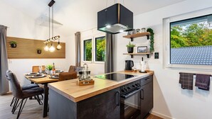 A modern kitchen with a central island, built-in oven, and a dining area with chairs and a table. - Vacation Home "14" with Private Terrace & Wi-Fi (Bad Arolsen)