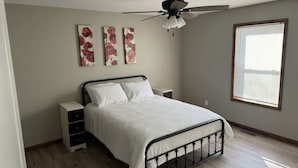 A bedroom with a bed, nightstands, a ceiling fan, and artwork on the wall.