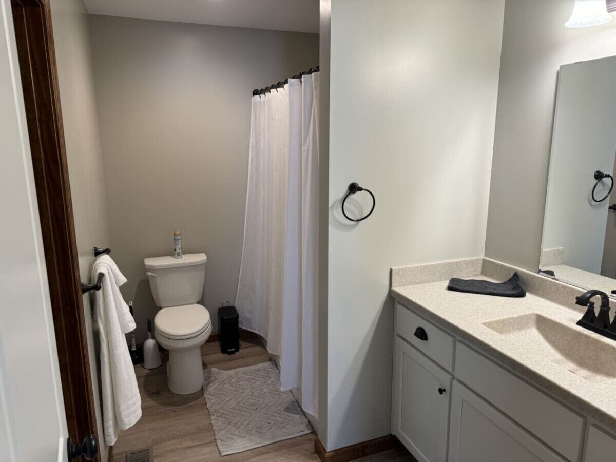 A bathroom with a toilet, shower curtain, sink, and mirror.