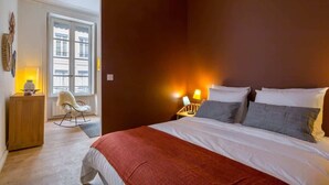 A bedroom with a bed, bedside lamps, a chair, a window, and a door. - Patchwork - Furnished apartment - Downtown Lyon (Lyon)