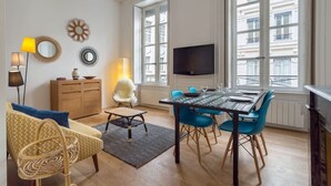 A modern living room with a dining area, large windows, and a flat-screen TV. - Patchwork - Furnished apartment - Downtown Lyon (Lyon)
