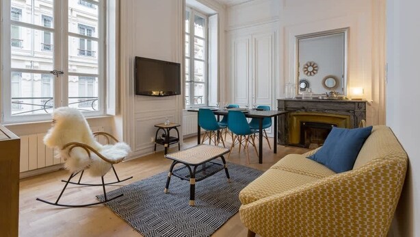 A living room with a sofa, a rocking chair, a TV, a fireplace, and a dining area with chairs. - Patchwork - Furnished apartment - Downtown Lyon (Lyon)