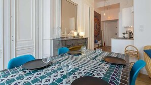 A dining area with a tiled table, chairs, a fireplace, and a kitchen in the background. - Patchwork - Furnished apartment - Downtown Lyon (Lyon)