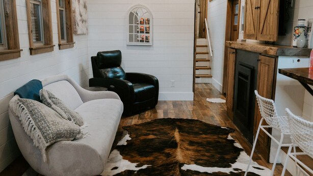 Un salon chaleureux avec un canapé blanc, un fauteuil en cuir noir et un tapis en peau de vache.