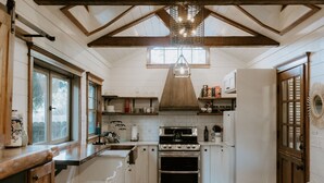 A kitchen with white cabinets, a stove, and a sink. There are windows and a ceiling fan. - Creekside Under the Redwoods (Guerneville)