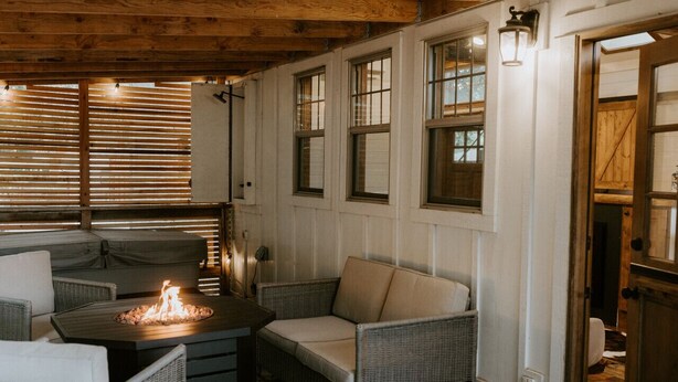 A cozy indoor seating area with wicker furniture, a fire feature, and large windows. - Creekside Under the Redwoods (Guerneville)