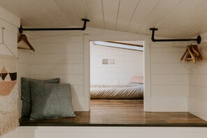 A room with a sloped ceiling, wooden beams, a bed with a pink pillow, and a hanging wooden rack. - Creekside Under the Redwoods (Guerneville)