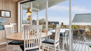 Un coin repas avec une table ronde en bois, des chaises blanches dotées d’assises rembourrées et un luminaire suspendu.