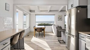 Una cocina moderna con vista al océano, un comedor con mesa y sillas, y un refrigerador empotrado.