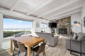A spacious living area with a wooden dining table, grey sofas, and a stone fireplace.
