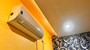 Un condizionatore d'aria fissato al muro in una stanza con pareti gialle e un rivestimento decorativo a motivi bianchi e neri.