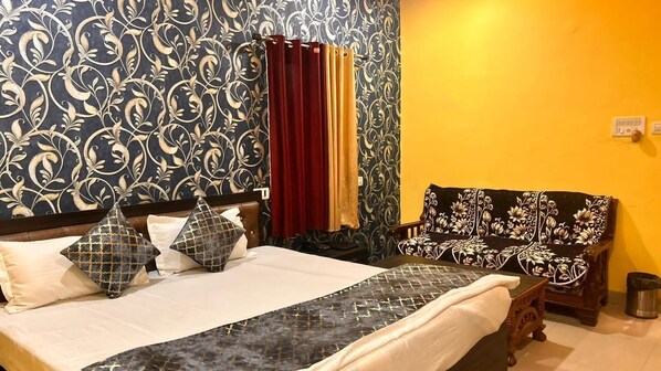 A hotel room with a bed, a sofa, patterned wallpaper, and curtains. - Hotel Chandrawali (Ballia)