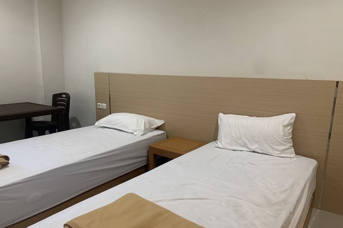 Una habitación con dos camas individuales, un cabecero de madera, una mesita de madera y una silla.