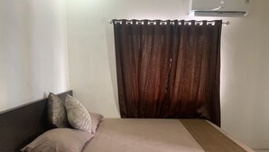 Una cama bien hecha con una colcha marrón y dos almohadas, un cabecero oscuro y una cortina marrón.