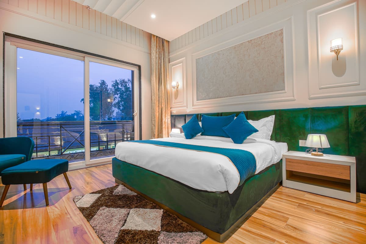 Ein modernes Schlafzimmer mit einem großen Bett, einem Nachttisch, einem Sessel und Blick ins Freie durch eine Schiebetür.