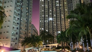 A nighttime view of a high-rise building with multiple balconies and a swimming pool area with palm trees and lights. - High-Tech Studio @ Grass Residences -2persons only (Quezon City)