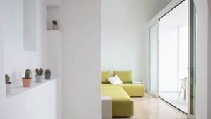 Een moderne woonkamer met een groene bank, een klein tafeltje en een potplant aan een witte muur.
