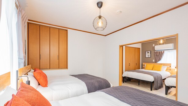 A bedroom with two beds, wooden wardrobes, a ceiling light, and a mirror. - ONCE Shinimamiya (Osaka)