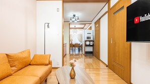 A modern living room with a sofa, a wooden coffee table with a vase, a flat-screen TV, and a kitchen in the background. - ONCE Shinimamiya (Osaka)