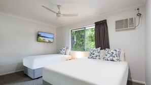 A bedroom with a bed, a smaller bed, a ceiling fan, a window with curtains, an air conditioning unit, and a TV on the wall.