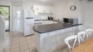 A modern kitchen with white cabinets, a granite countertop, a stainless steel microwave, and a wooden dining table with white chairs.