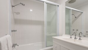 A modern bathroom with a glass-enclosed shower, a white bathtub, and a vanity with a sink and mirror.