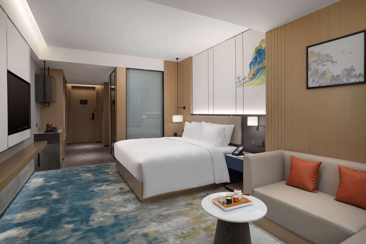 Een moderne hotelkamer met een groot bed, een bank, een televisie en een schilderij aan de muur.