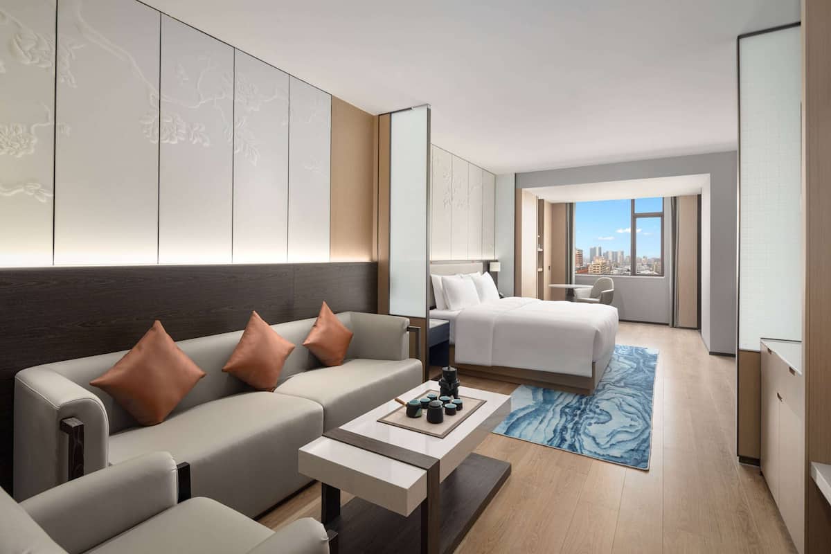 Een moderne hotelkamer met een bank, een bed, een bureau en uitzicht op de stad.