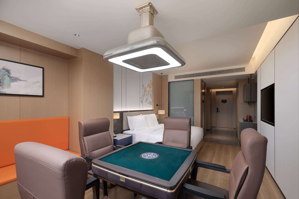 Een hotelkamer met een pooltafel, leren fauteuils, een bed met witte lakens, een televisie en een schilderij aan de muur.