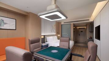 Una habitación de hotel con mesa de billar, sillones de cuero, cama con ropa blanca, televisor y un cuadro en la pared.