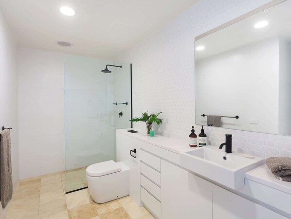 A modern bathroom with a glass shower enclosure, a white toilet, a vanity with a mirror, and a sink.