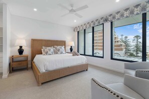 Ein Schlafzimmer mit einem Bett, zwei Nachttischen, einem Deckenventilator, einem großen Fenster mit Blick und einem Sessel.