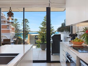 A modern kitchen with a view of a pool and buildings, a hanging light fixture, and a bowl of green apples.