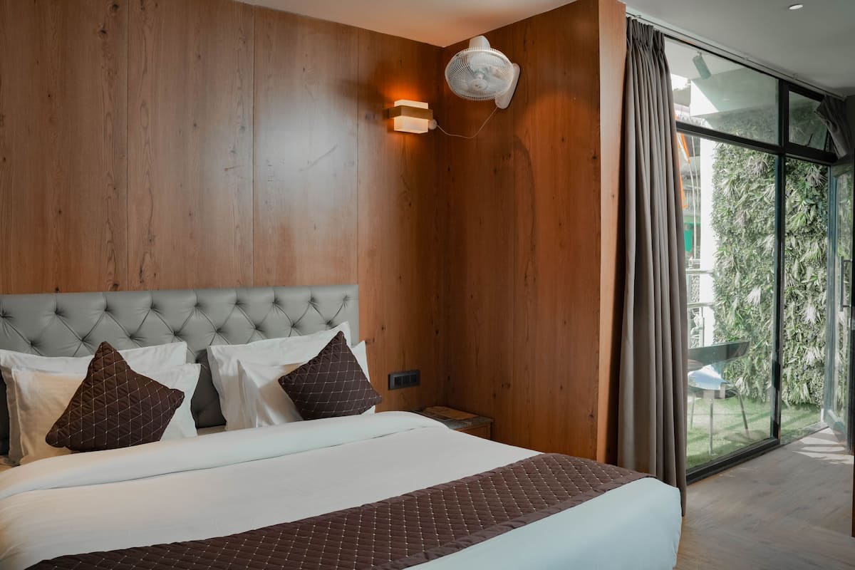 A bedroom with a large bed, wooden panel walls, a wall-mounted fan, and a sliding glass door leading to a balcony.