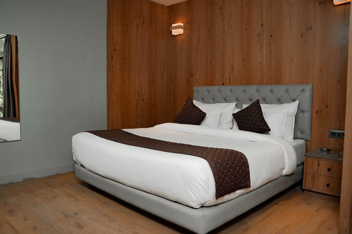 A modern bedroom with a large bed, wooden panel walls, and a nightstand.