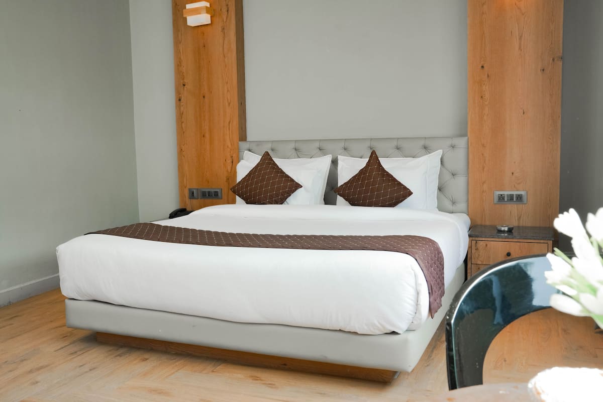 A large bed with a tufted headboard, two pillows, and a bedside table with a lamp.