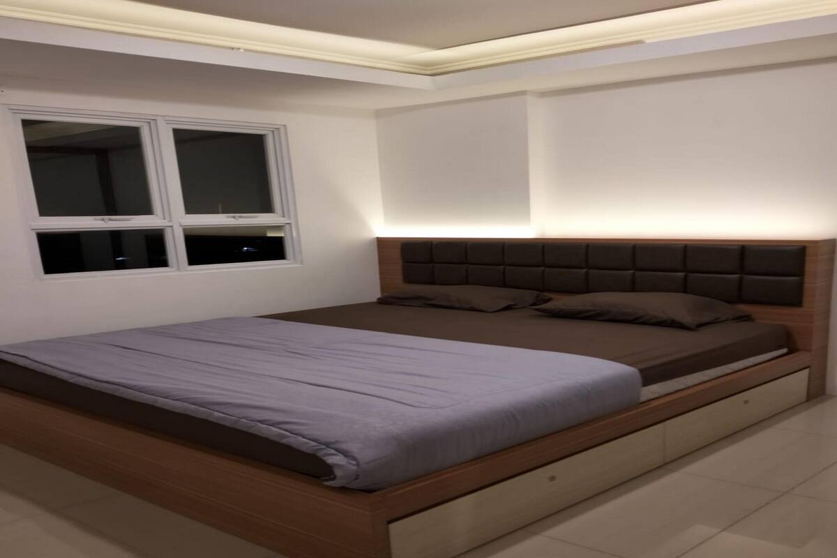 Een slaapkamer met een bed, een raam en een hoofdbord met ingebouwde verlichting.