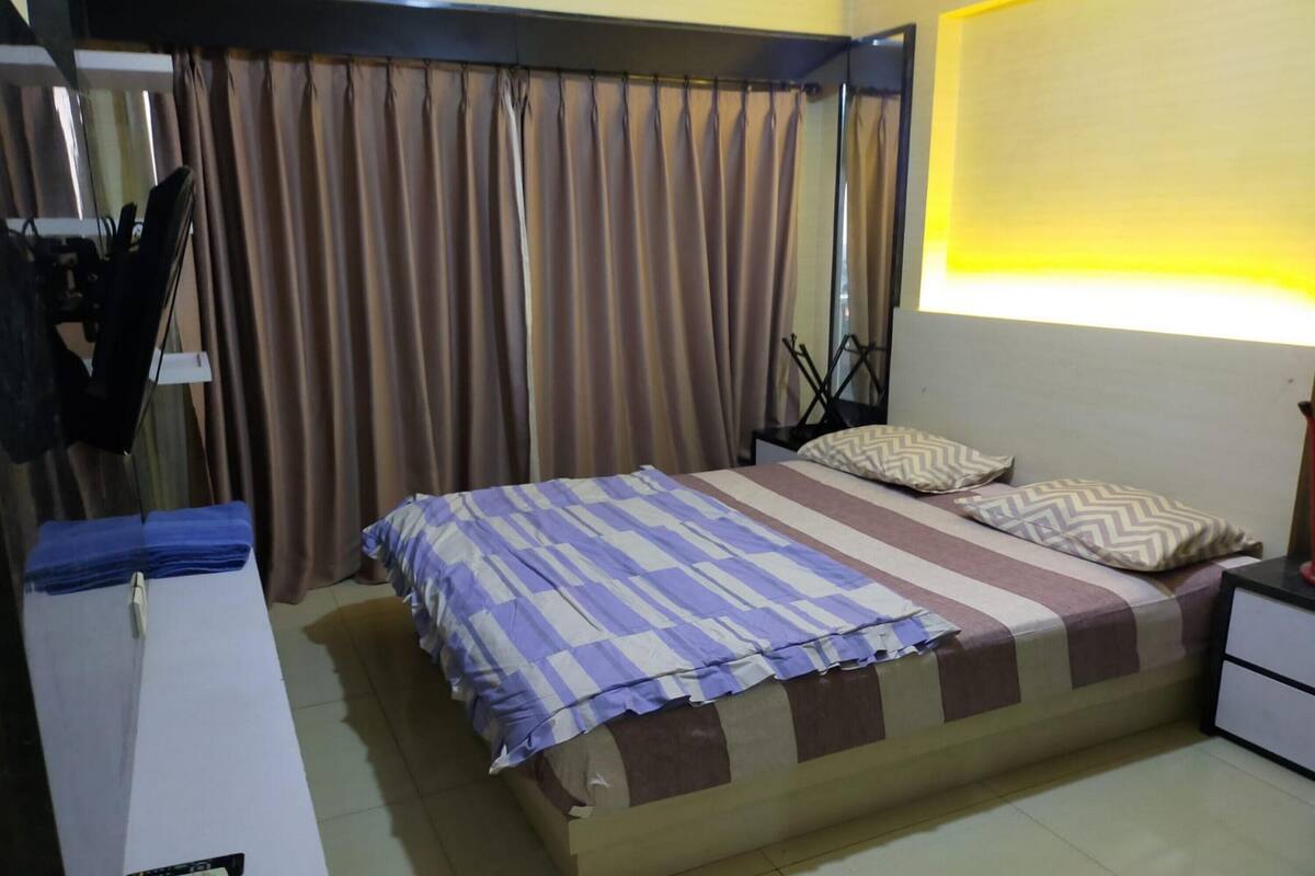 Een slaapkamer met een bed, gordijnen, een nachtkastje en een lamp.