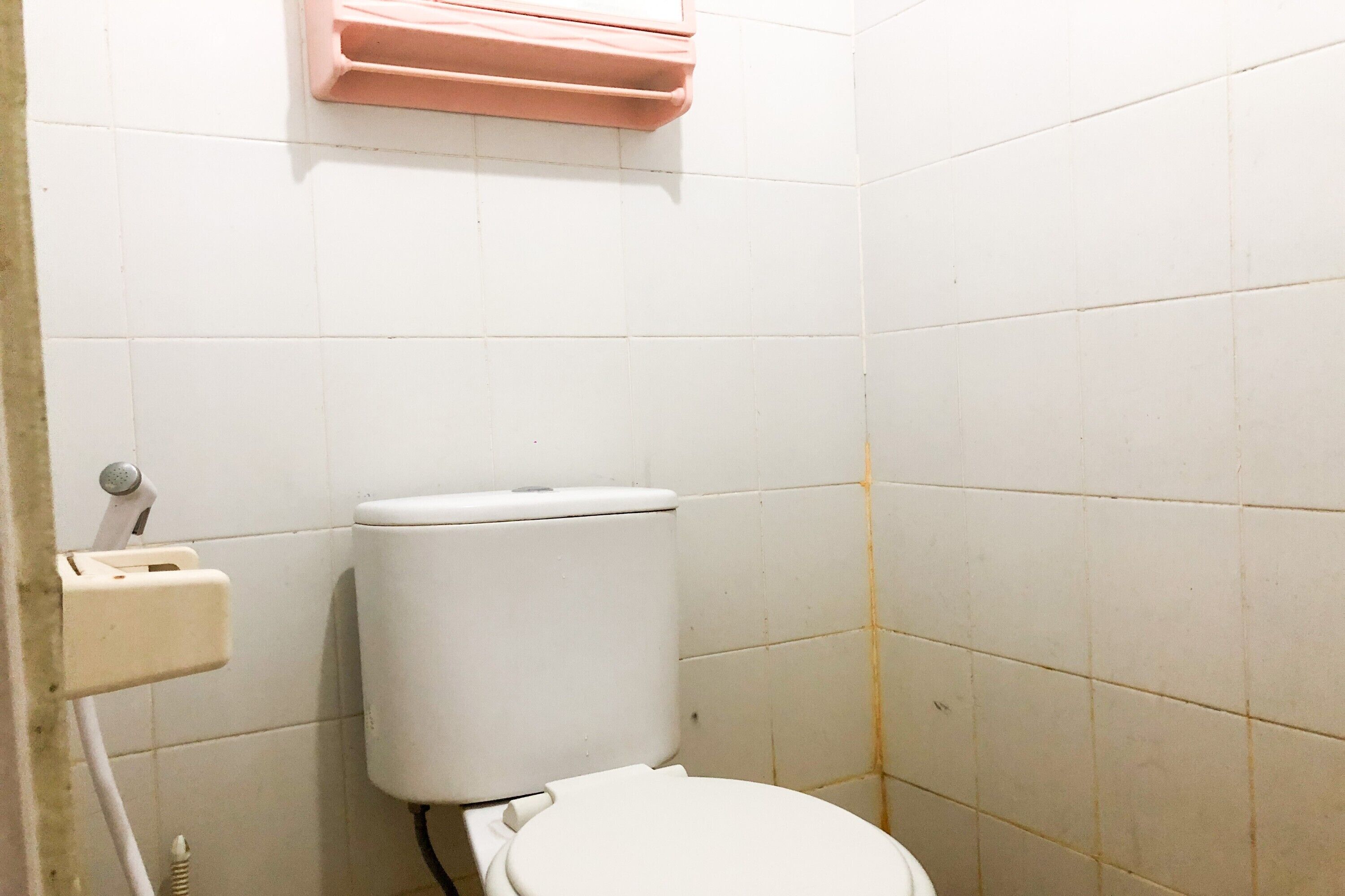 A small, basic bathroom with a white toilet, a pink soap dispenser, and a white toilet paper holder.