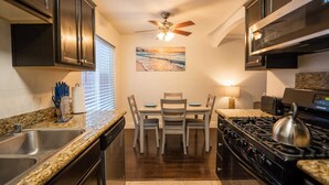 A compact kitchen with granite countertops, a gas stove, a ceiling fan, and a dining table with chairs.