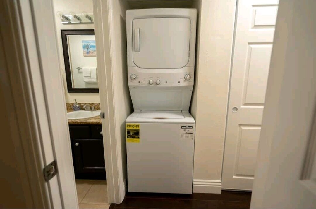 Una lavadora y secadora compactas en un pequeño cuarto de lavado, con un lavabo y un espejo arriba.