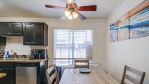 A kitchen with dark cabinets, a dishwasher, a coffee maker, and a dining table with chairs.
