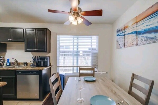 A kitchen with dark cabinets, a dishwasher, a coffee maker, and a dining table with chairs.