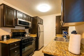 A kitchen with dark cabinets, a stainless steel refrigerator, a microwave, a stove, and granite countertops.