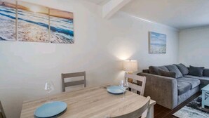 A dining area with a wooden table and chairs, a sofa, and wall art depicting a beach scene.