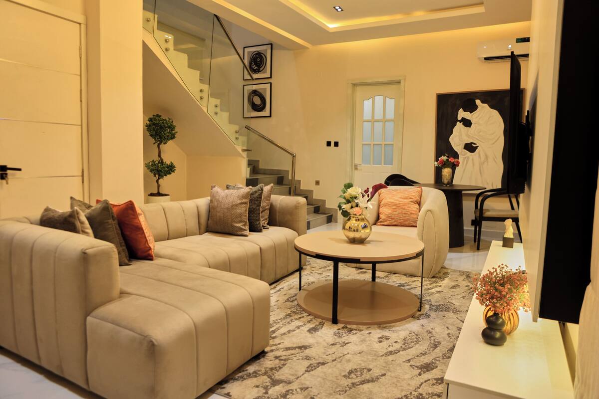 A modern living room with a beige sofa, a coffee table, and a staircase leading to an upper floor.