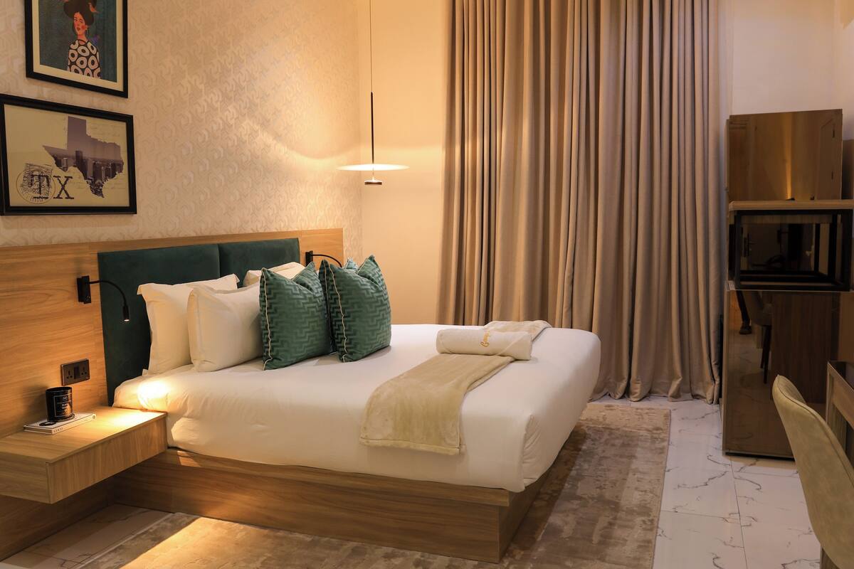 A neatly made bed with pillows and a blanket, a bedside table with a lamp, and a wall with framed artwork.