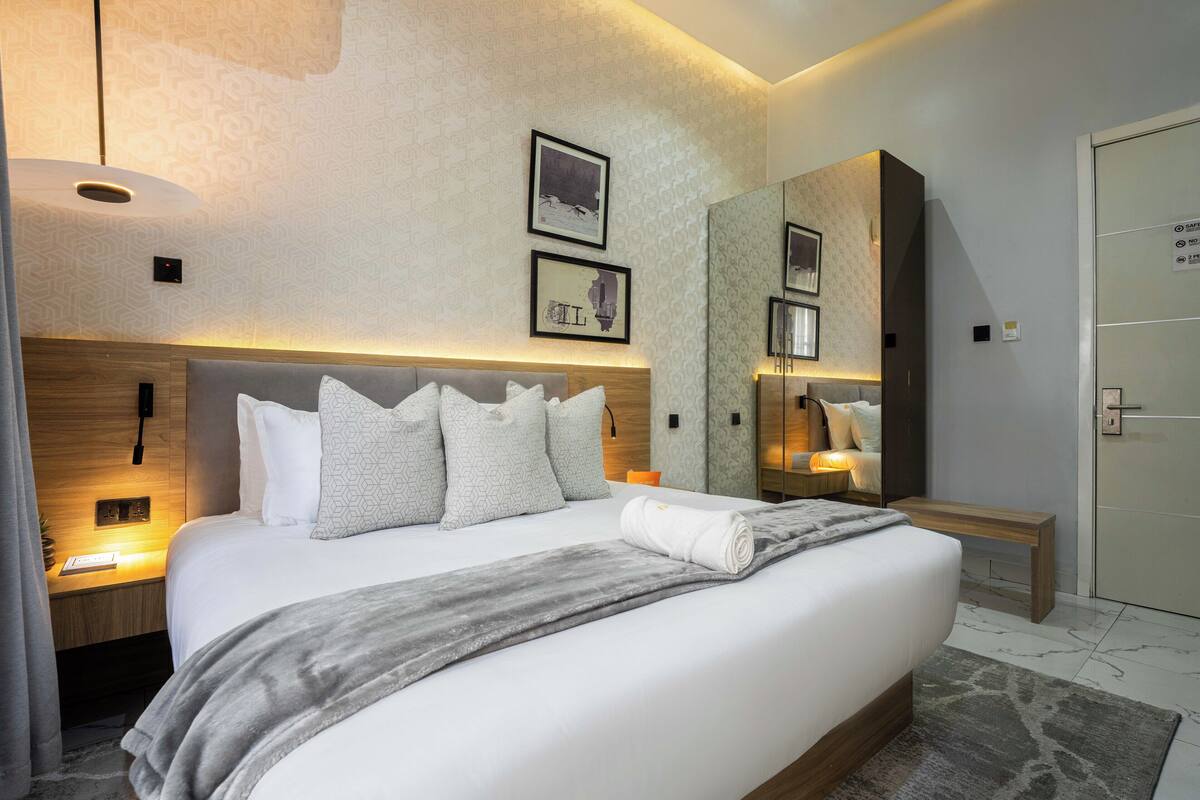 A modern hotel room with a large bed, bedside tables, a mirror, and a wardrobe.