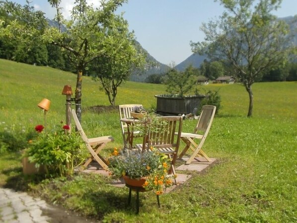 Un jardín con una mesa y sillas de madera, rodeado de flores y plantas.