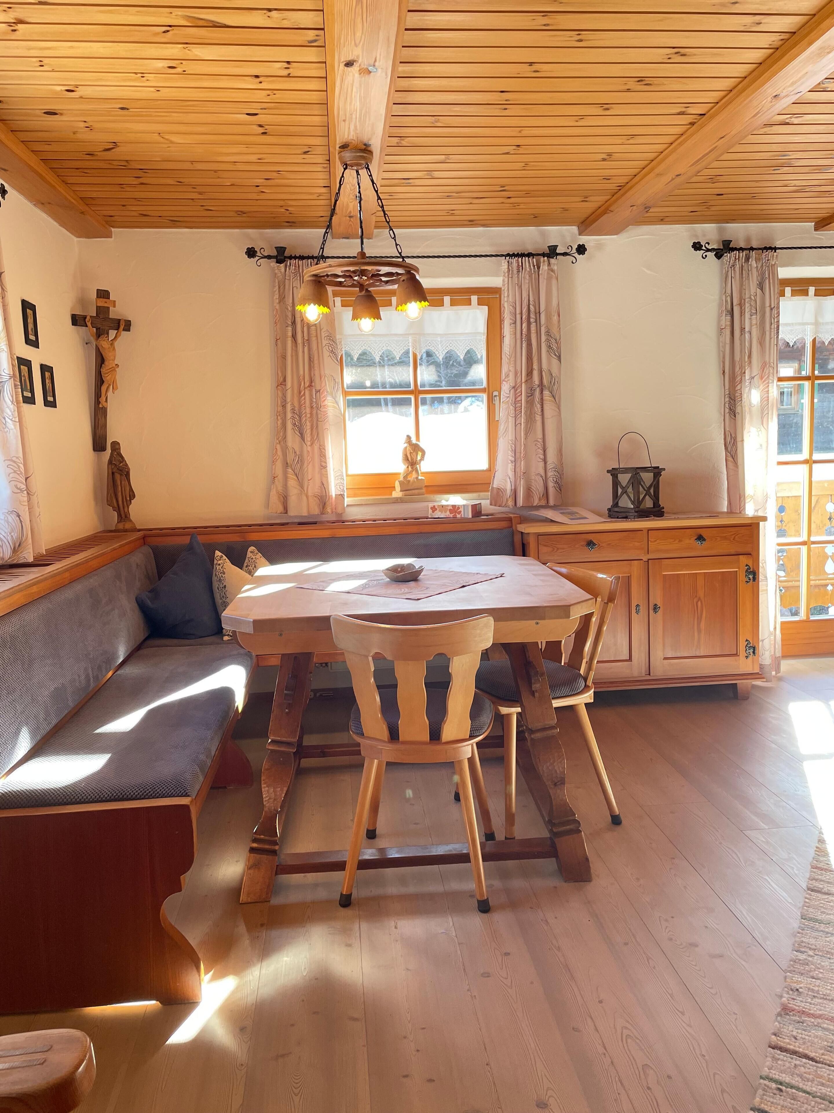 Een gezellig eetgedeelte met een houten tafel en stoelen, een bank en een kruis aan de muur.